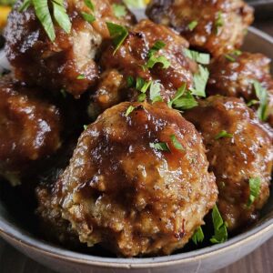 Meatballs covered in sauce and chopped parsley in a light-colored bowl.