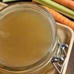 Chicken broth in a glass mason jar next to carrots and celery.