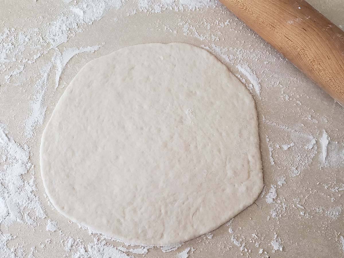 Pita dough rolled out on a floured counter.