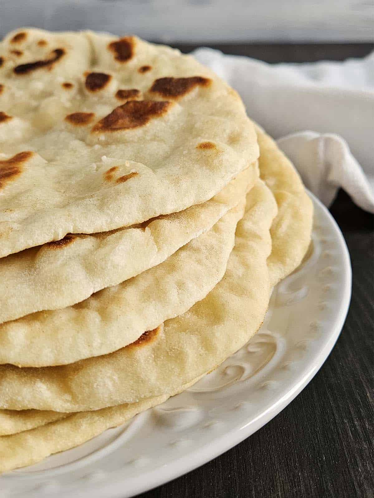 Six pieces of sourdough flatbread stacked on a white plate.