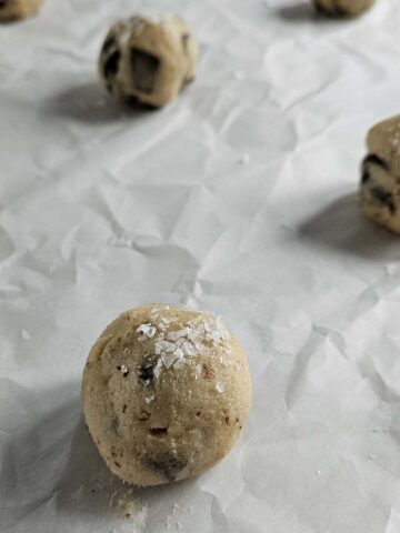 Chocolate chip cookie dough balls sprinkled with salt on parchment paper.