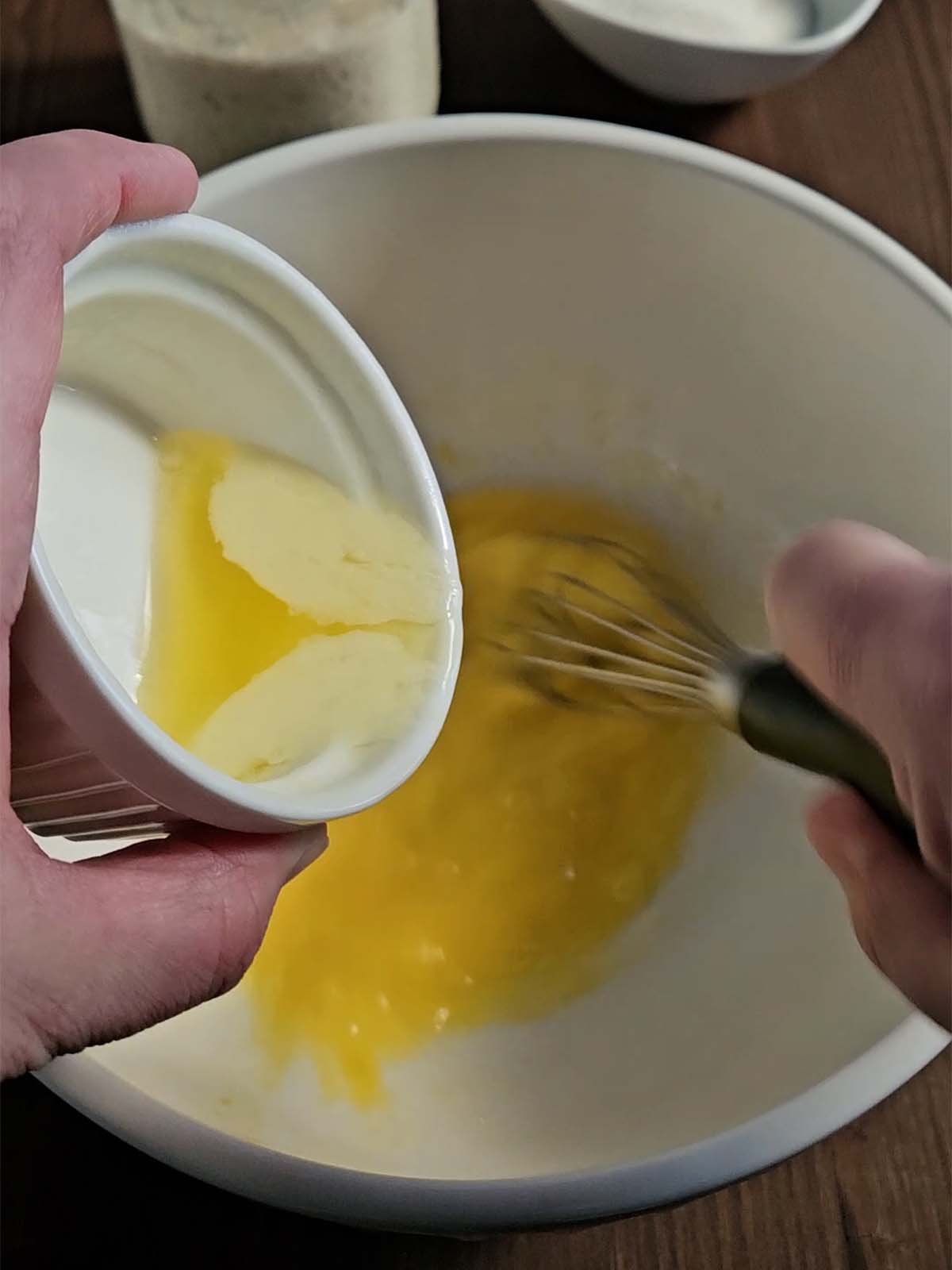 Pouring melted butter in to a white bowl filled with whisked eggs.
