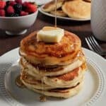 Stack of pancakes topped with butter and syrup on a white plate.