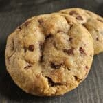 Two chocolate chip peanut butter cookies on a dark wood surface.