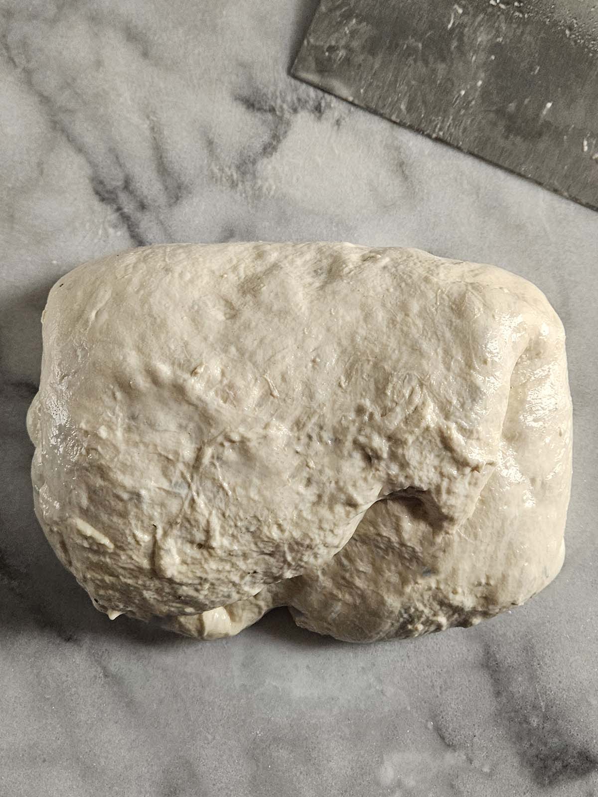 Dough folded into a round on a white marble surface.