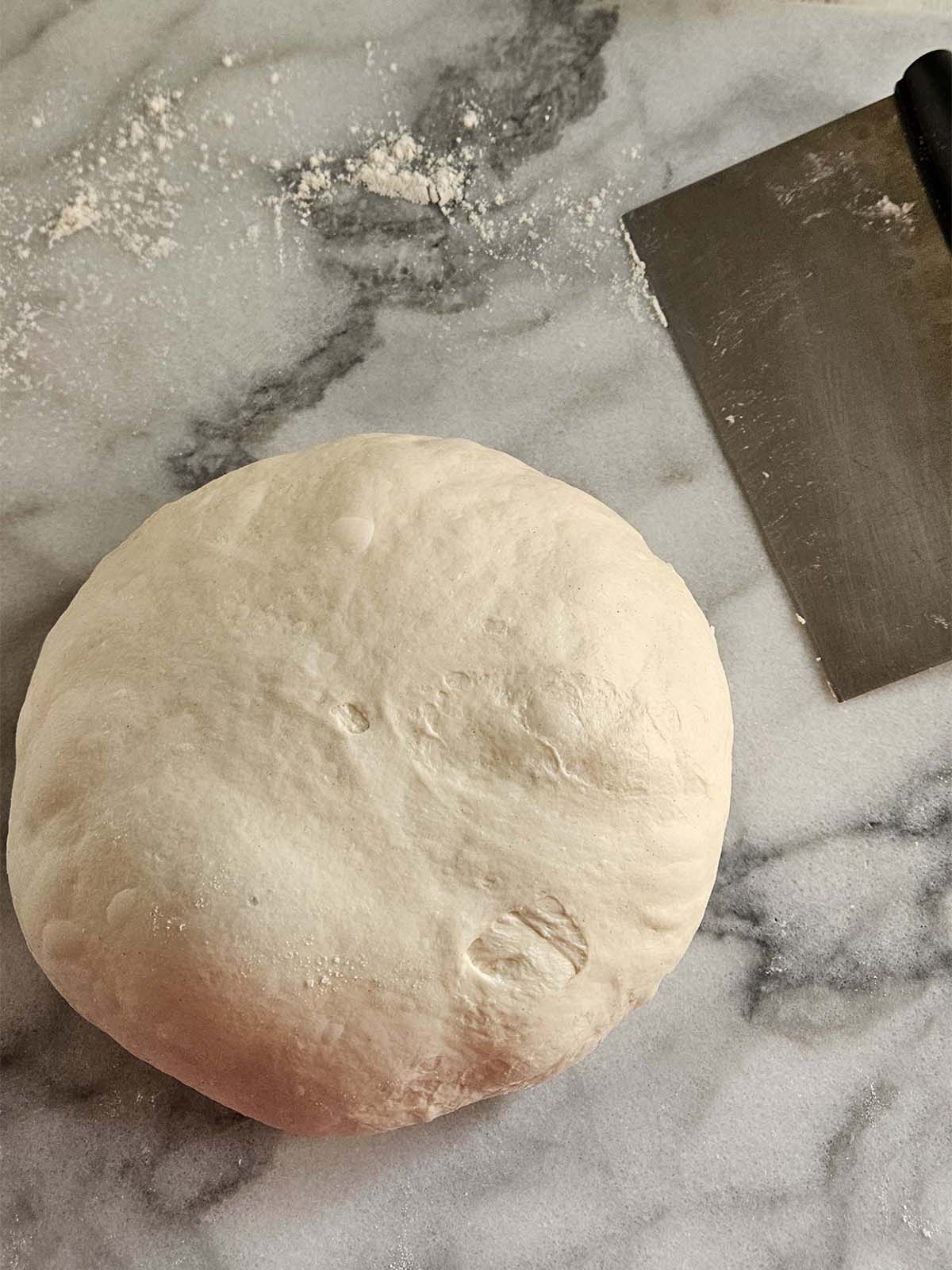 Shaped round of sourdough on white marble.