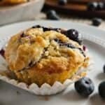 Sourdough Blueberry Muffin on a white plate surrounded by blueberries.