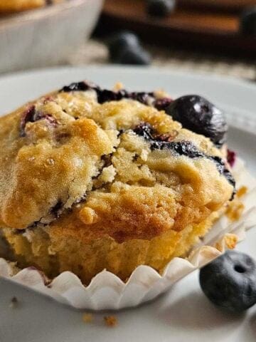 Sourdough Blueberry Muffin on a white plate surrounded by blueberries.